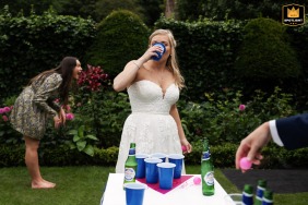 Eine Braut spielt Bier Pong auf dem üppig grünen Rasen von Chenies Manor in Buckinghamshire, ein lustiger und einzigartiger Moment an ihrem Hochzeitstag.